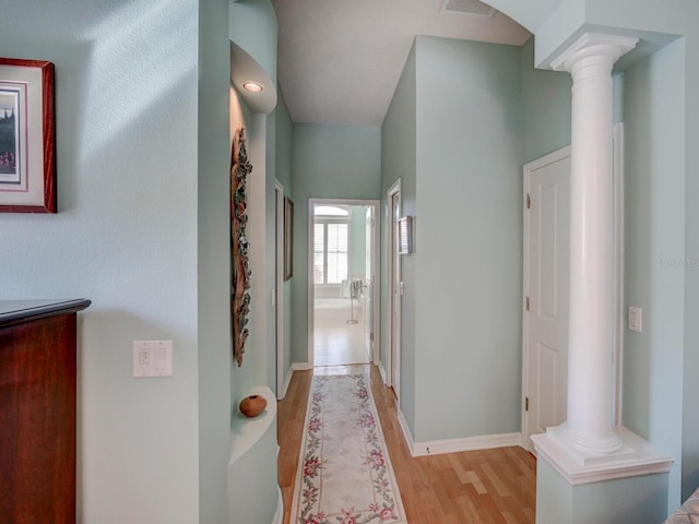 hallway featuring baseboards, light wood-style floors, visible vents, and ornate columns