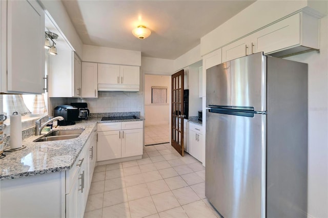 kitchen with black electric stovetop, backsplash, freestanding refrigerator, white cabinetry, and a sink