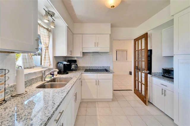 kitchen with black electric stovetop, under cabinet range hood, a sink, white cabinets, and tasteful backsplash