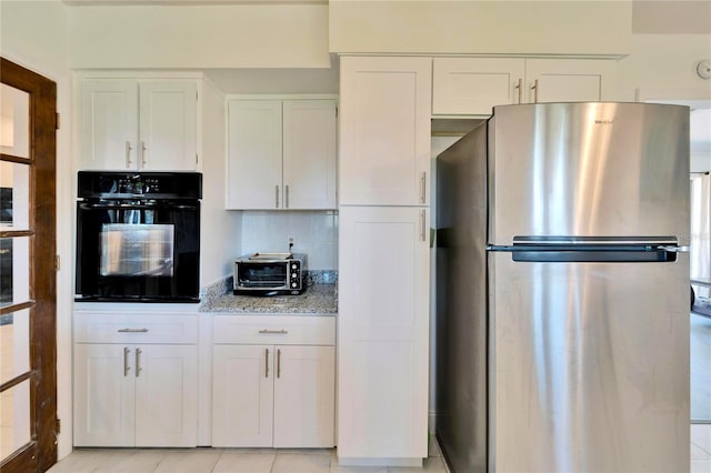 kitchen with oven, tasteful backsplash, white cabinetry, and freestanding refrigerator