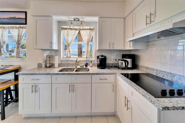 kitchen featuring light stone counters, backsplash, a sink, under cabinet range hood, and black electric cooktop