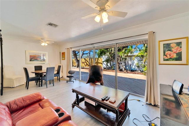 living room featuring ornamental molding, light wood-type flooring, visible vents, and a ceiling fan