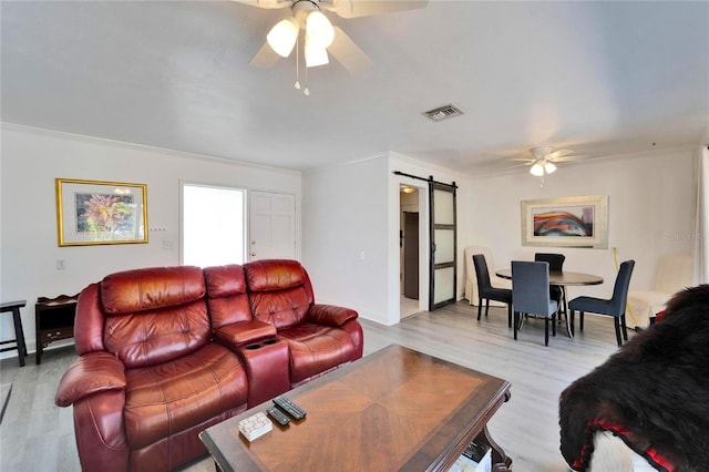 living room featuring a barn door, visible vents, light wood-style flooring, and a ceiling fan