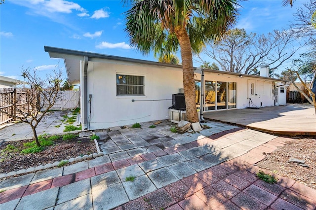 view of front of house with stucco siding, a fenced backyard, a chimney, and a wooden deck