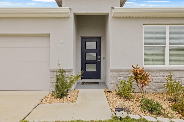 entrance to property with a garage, stone siding, and stucco siding