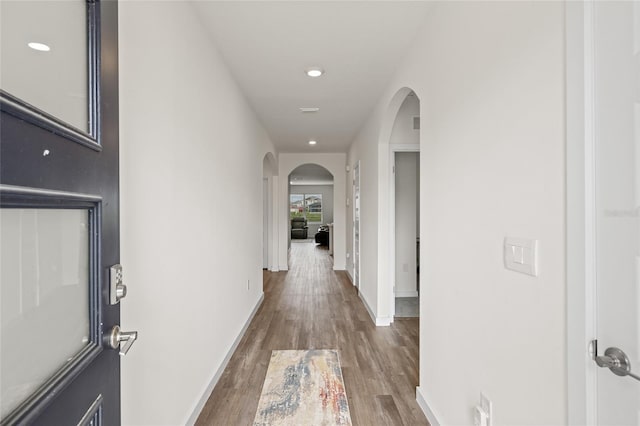 hallway with baseboards, arched walkways, wood finished floors, and recessed lighting