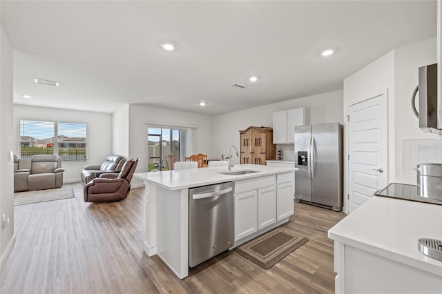 kitchen with stainless steel appliances, a sink, white cabinets, light countertops, and an island with sink