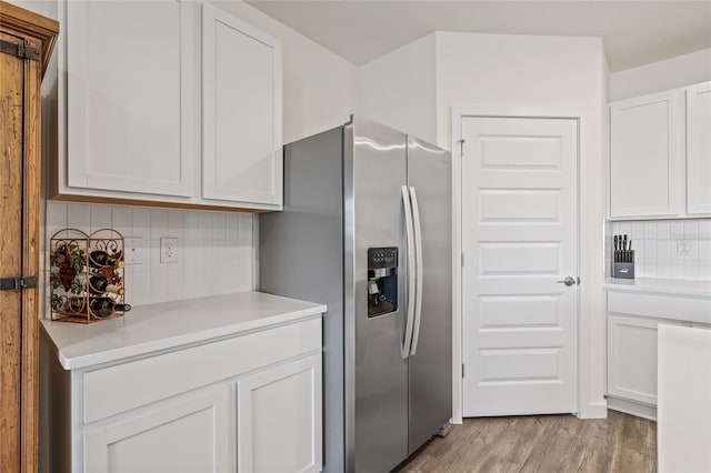 kitchen with white cabinetry, light wood-style floors, light countertops, stainless steel refrigerator with ice dispenser, and decorative backsplash