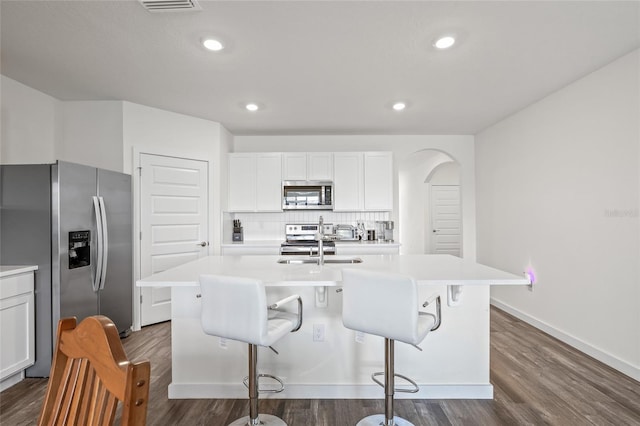 kitchen featuring arched walkways, light countertops, appliances with stainless steel finishes, and tasteful backsplash