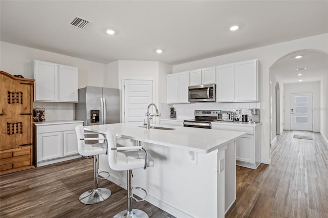 kitchen featuring arched walkways, dark wood-type flooring, a sink, visible vents, and appliances with stainless steel finishes