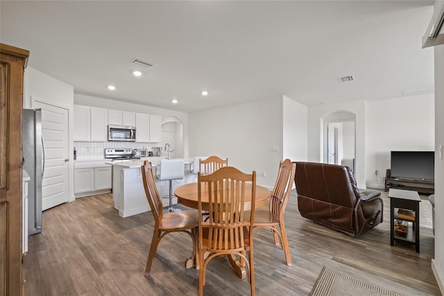 dining room with arched walkways, visible vents, recessed lighting, and wood finished floors