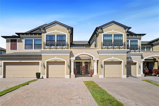 multi unit property featuring decorative driveway, a balcony, an attached garage, and stucco siding