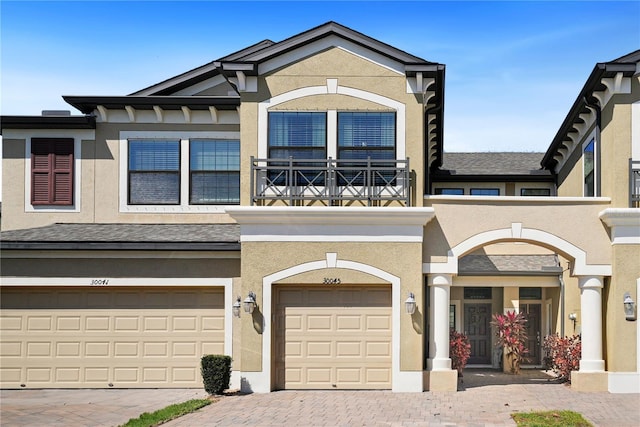 view of front of home with stucco siding, an attached garage, decorative driveway, and a balcony