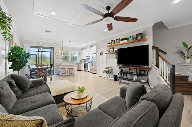 living room with visible vents, ornamental molding, a ceiling fan, light wood-style flooring, and stairway