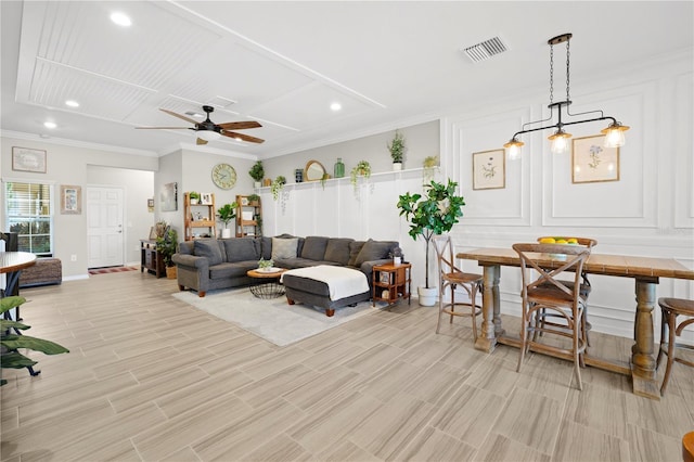 living room with a decorative wall, visible vents, crown molding, and ceiling fan