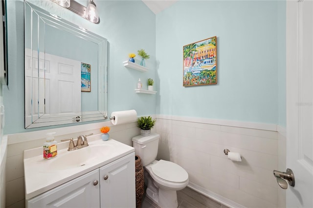 half bath featuring a wainscoted wall, toilet, tile walls, and vanity