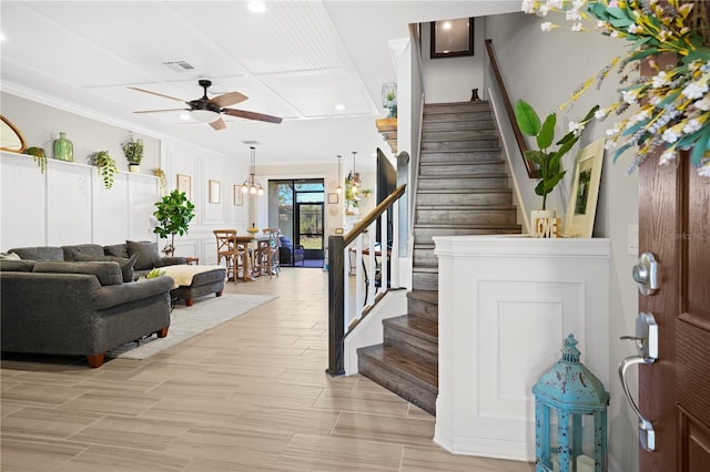 interior space featuring visible vents, ornamental molding, a ceiling fan, a decorative wall, and stairs