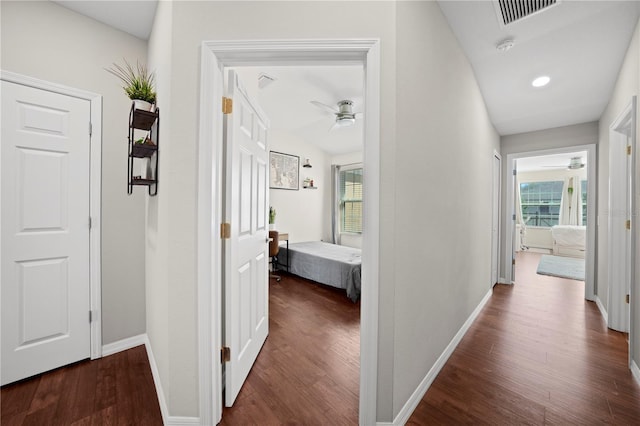 hall with visible vents, baseboards, and wood finished floors