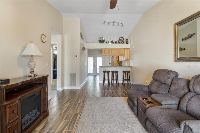 living area with wood finish floors, lofted ceiling, visible vents, rail lighting, and baseboards