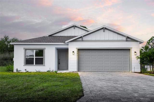 ranch-style house featuring an attached garage, roof with shingles, decorative driveway, a front lawn, and board and batten siding