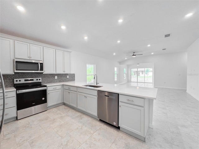 kitchen featuring stainless steel appliances, light countertops, decorative backsplash, a sink, and a peninsula