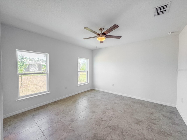 empty room with baseboards, a textured ceiling, visible vents, and a ceiling fan