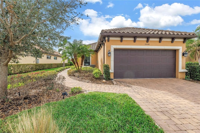 mediterranean / spanish-style home featuring a garage, a tile roof, decorative driveway, and stucco siding