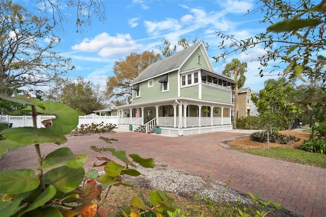 farmhouse inspired home with covered porch, decorative driveway, and fence