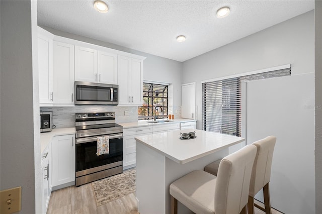 kitchen featuring a sink, light countertops, appliances with stainless steel finishes, light wood finished floors, and tasteful backsplash