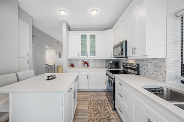 kitchen featuring white cabinets, glass insert cabinets, stainless steel appliances, light countertops, and light wood-style floors