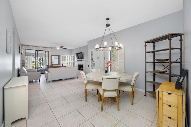 dining room featuring ceiling fan with notable chandelier, a fireplace, baseboards, and light tile patterned floors