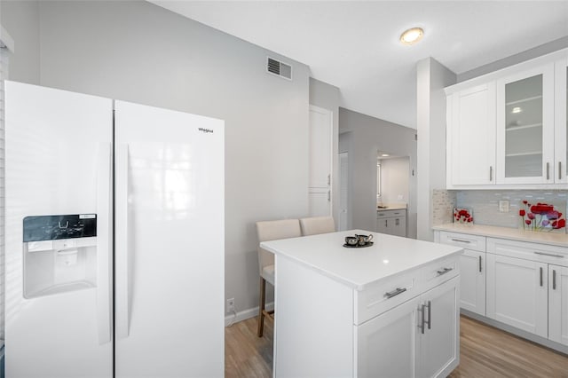 kitchen featuring white refrigerator with ice dispenser, light countertops, visible vents, backsplash, and glass insert cabinets