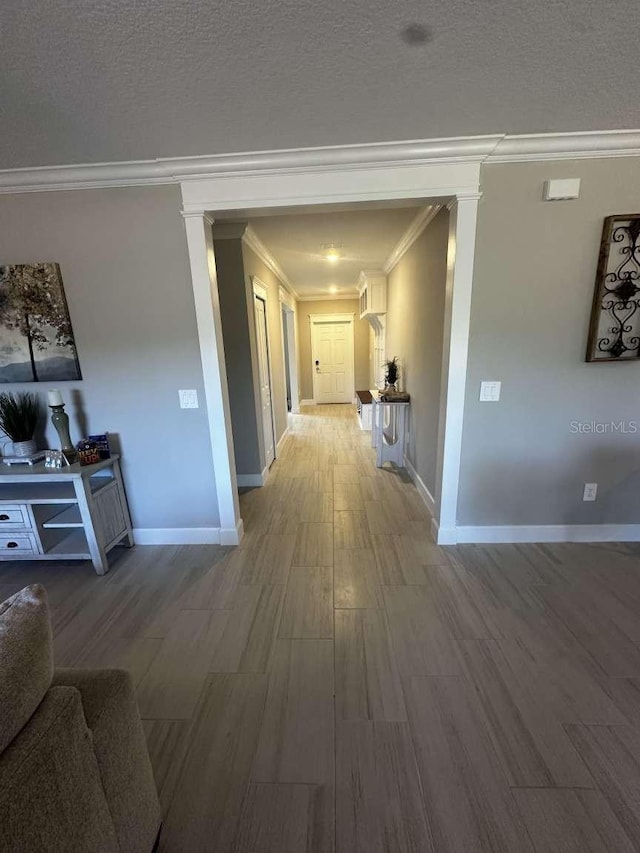 corridor with decorative columns, light wood-style floors, baseboards, and a textured ceiling