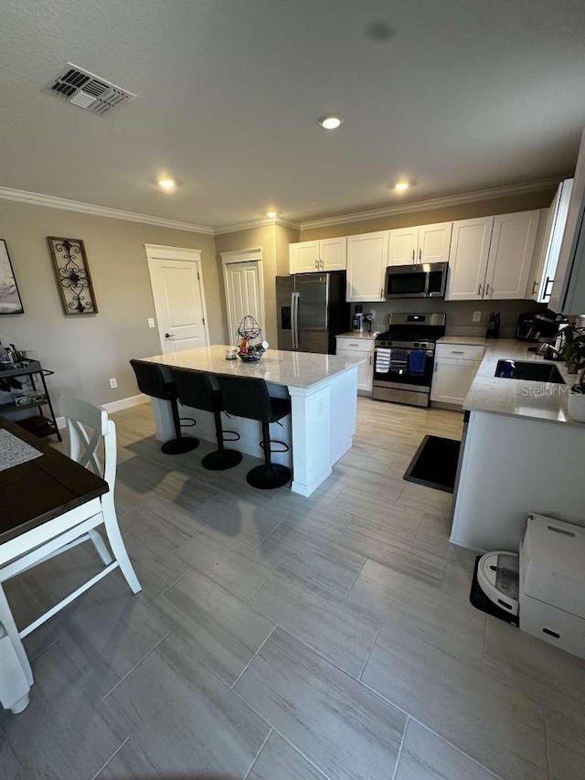 kitchen featuring visible vents, crown molding, a breakfast bar area, appliances with stainless steel finishes, and a sink