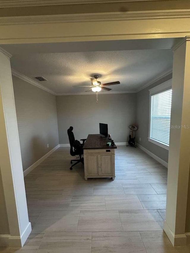 unfurnished office featuring visible vents, ornamental molding, a textured ceiling, baseboards, and ceiling fan