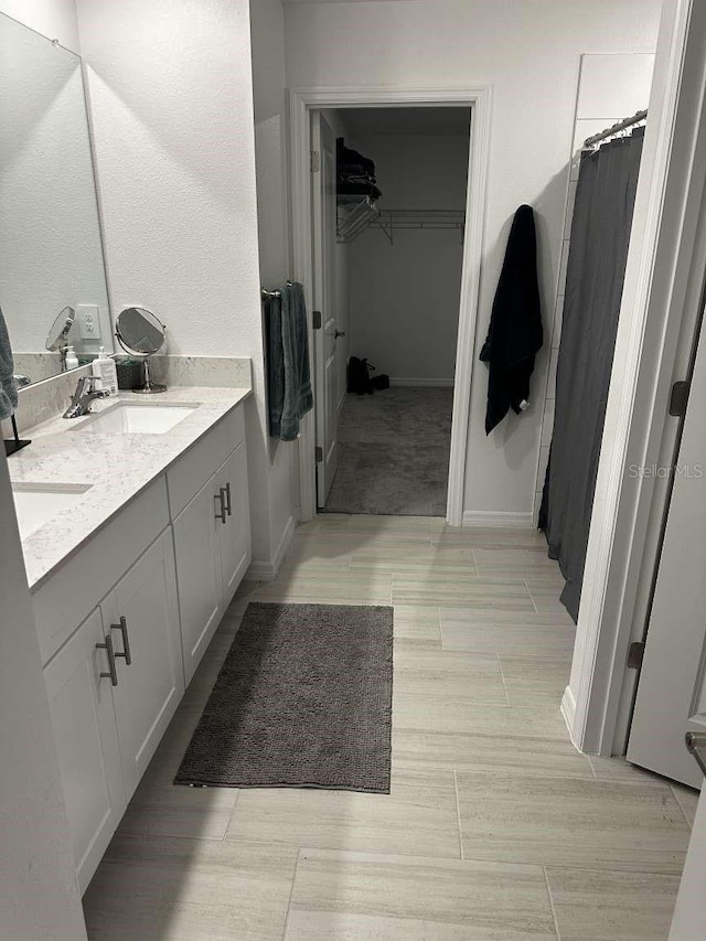 bathroom featuring a shower with curtain, a sink, double vanity, baseboards, and a spacious closet