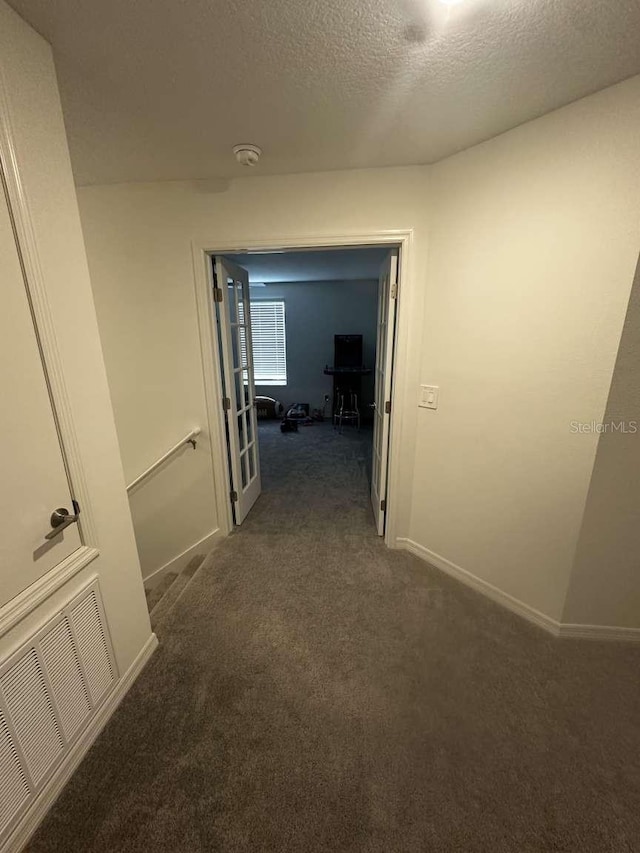 hallway featuring dark colored carpet, visible vents, baseboards, and a textured ceiling