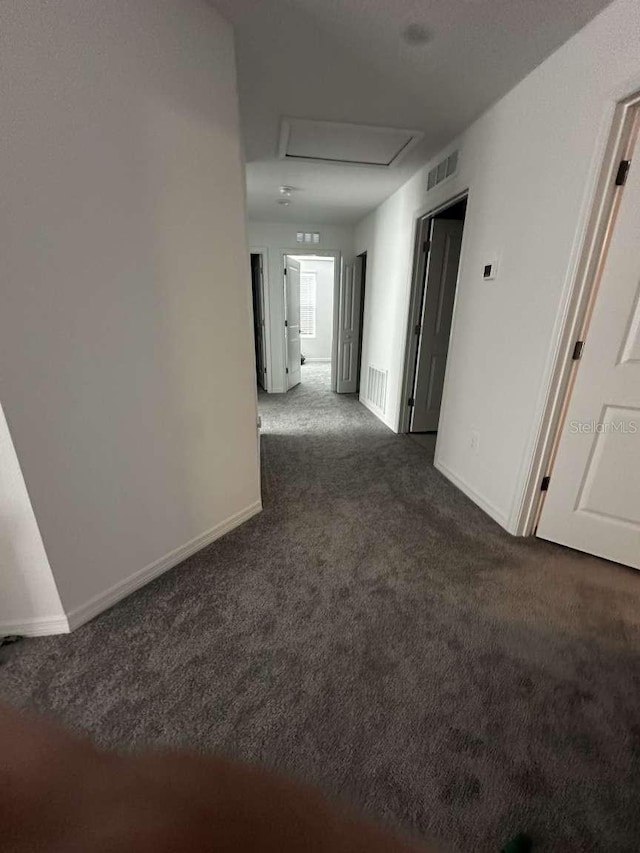 corridor with baseboards, visible vents, attic access, and carpet