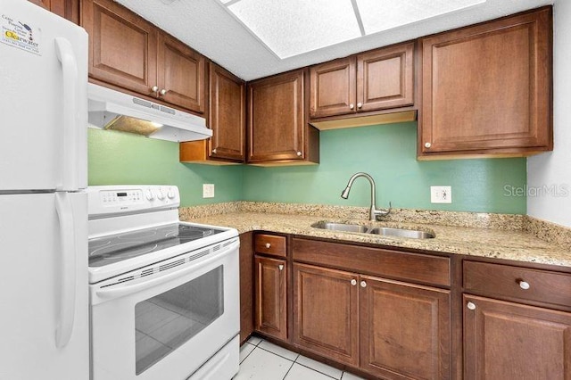 kitchen with light stone counters, under cabinet range hood, white appliances, a sink, and brown cabinetry