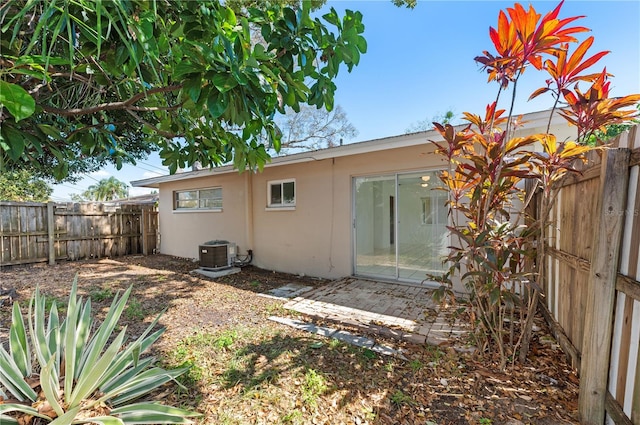 rear view of property with a fenced backyard, central AC, and stucco siding