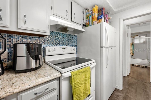 kitchen featuring under cabinet range hood, white appliances, dark wood-type flooring, white cabinets, and backsplash