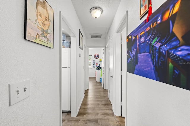 hall featuring attic access, a textured ceiling, wood finished floors, and a textured wall