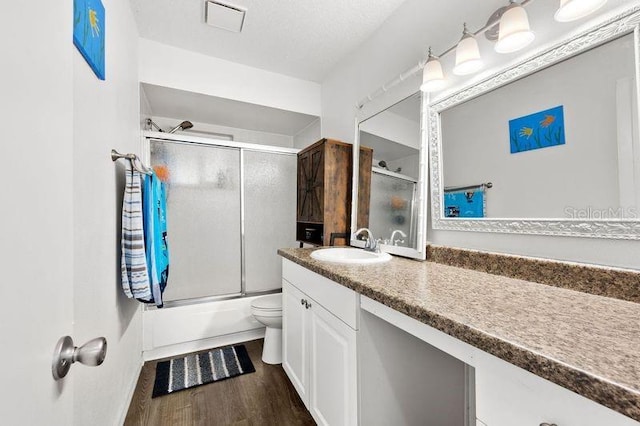 full bath featuring toilet, bath / shower combo with glass door, wood finished floors, visible vents, and vanity