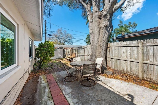 view of patio with an outbuilding, fence, outdoor dining space, and a shed