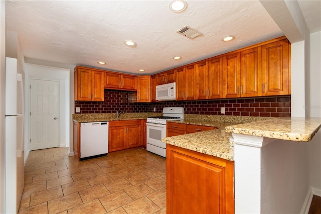 kitchen featuring visible vents, decorative backsplash, brown cabinetry, white appliances, and a peninsula