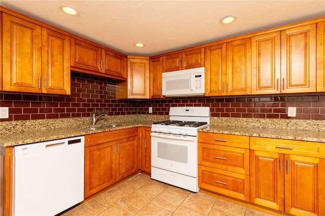 kitchen featuring white appliances, brown cabinetry, light stone counters, a sink, and backsplash