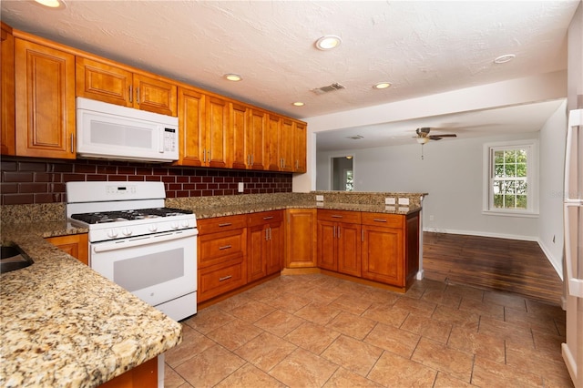 kitchen with brown cabinetry, white appliances, visible vents, and a peninsula