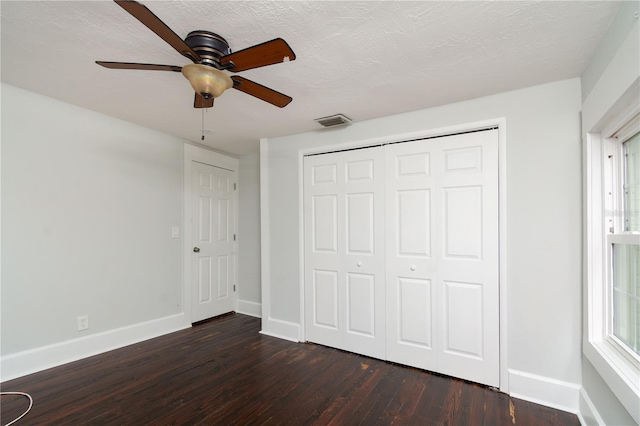 unfurnished bedroom with a textured ceiling, dark wood-style flooring, visible vents, baseboards, and a closet