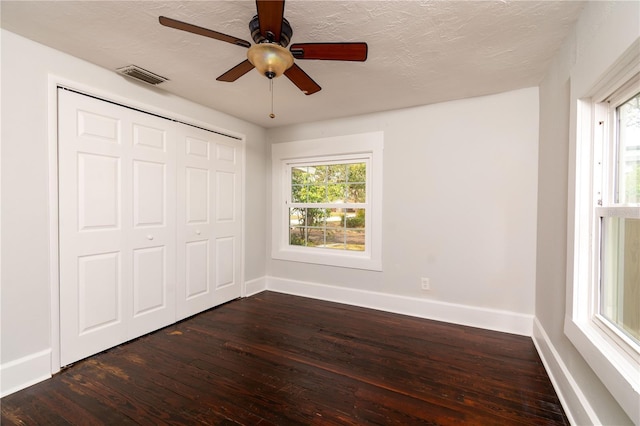 unfurnished bedroom with baseboards, multiple windows, visible vents, and dark wood finished floors