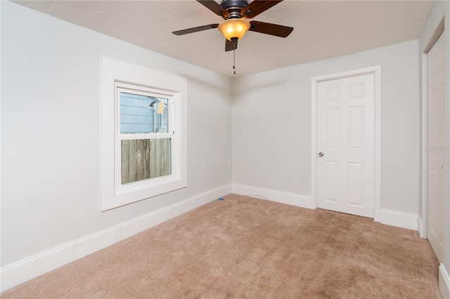 carpeted spare room featuring a ceiling fan and baseboards